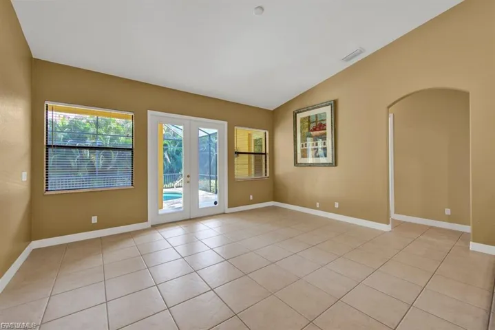 Empty room with vaulted ceiling, french doors, light tile patterned floors, and arched walkways