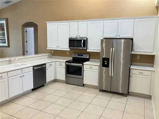 Kitchen featuring appliances with stainless steel finishes, light countertops, white cabinetry, arched walkways, and lofted ceiling