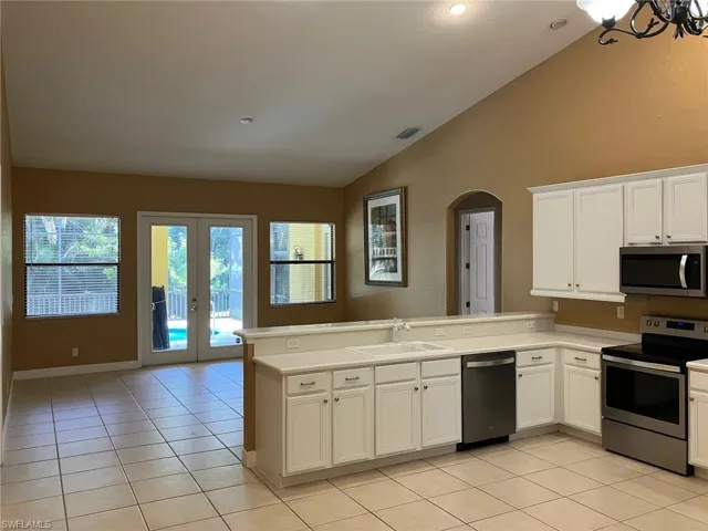 Kitchen featuring a peninsula, stainless steel appliances, vaulted ceiling, arched walkways, and light tile patterned floors