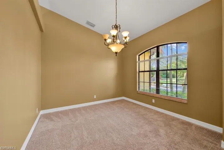 Carpeted empty room with lofted ceiling and a chandelier