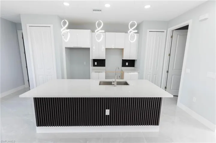 Kitchen featuring sink, an island with sink, hanging light fixtures, and white cabinets