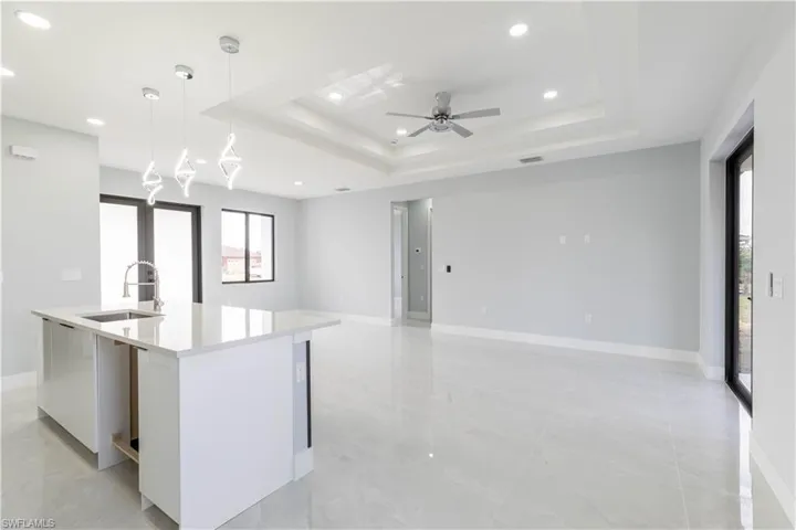 Kitchen featuring decorative light fixtures, sink, white cabinets, a raised ceiling, and a center island with sink