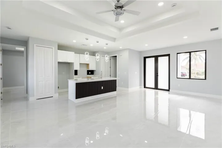 Kitchen with ceiling fan, white cabinetry, a tray ceiling, an island with sink, and french doors