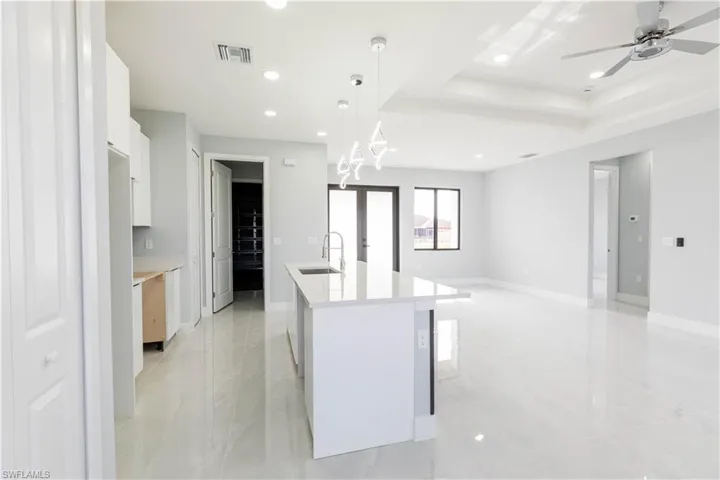 Kitchen featuring decorative light fixtures, an island with sink, sink, white cabinets, and a tray ceiling