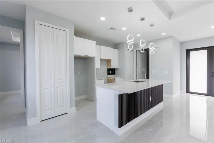 Kitchen with white cabinetry, sink, a kitchen island with sink, and pendant lighting