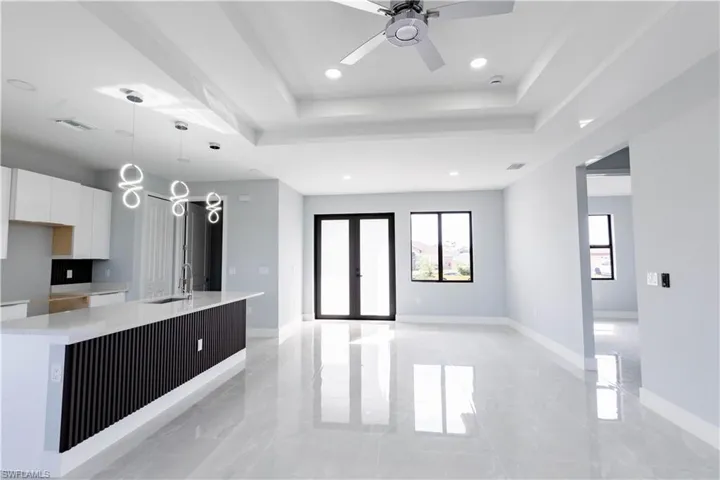 Kitchen with french doors, a raised ceiling, a center island with sink, and white cabinets