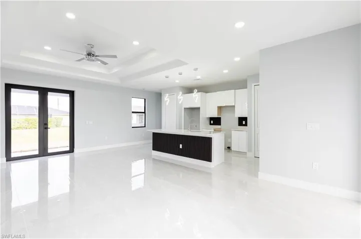 Kitchen with sink, white cabinetry, decorative light fixtures, a center island with sink, and a raised ceiling