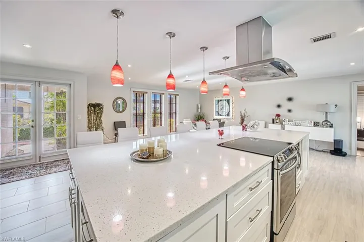 Kitchen featuring stainless steel electric range oven, island exhaust hood, light stone counters, and decorative light fixtures