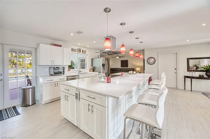 Kitchen with hanging light fixtures, stainless steel appliances, a kitchen breakfast bar, white cabinets, and a kitchen island