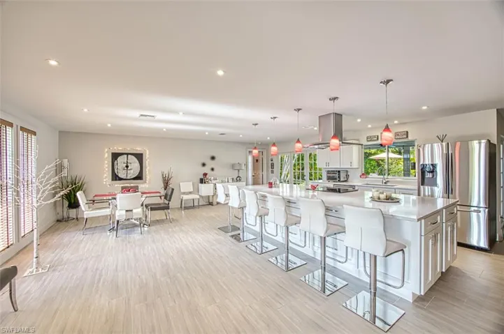 Kitchen with a large island, hanging light fixtures, white cabinets, and stainless steel refrigerator with ice dispenser