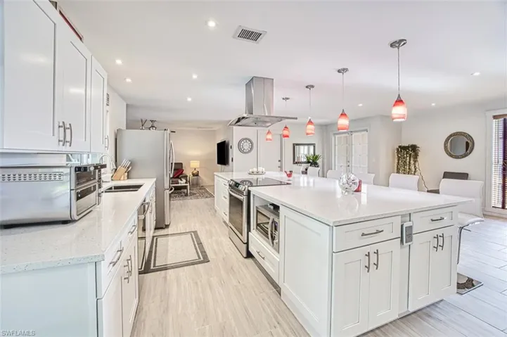 Kitchen featuring appliances with stainless steel finishes, island exhaust hood, white cabinets, a kitchen bar, and decorative light fixtures