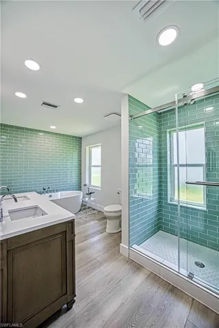 Bathroom featuring double vanity, a stall shower, recessed lighting, light wood-style floors, and a soaking tub