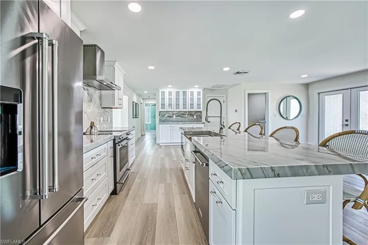 Kitchen featuring a kitchen breakfast bar, appliances with stainless steel finishes, white cabinetry, light wood-style floors, and wall chimney exhaust hood