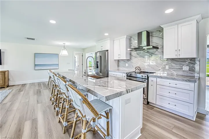 Kitchen with stainless steel appliances, a kitchen bar, light stone countertops, a center island with sink, and decorative backsplash