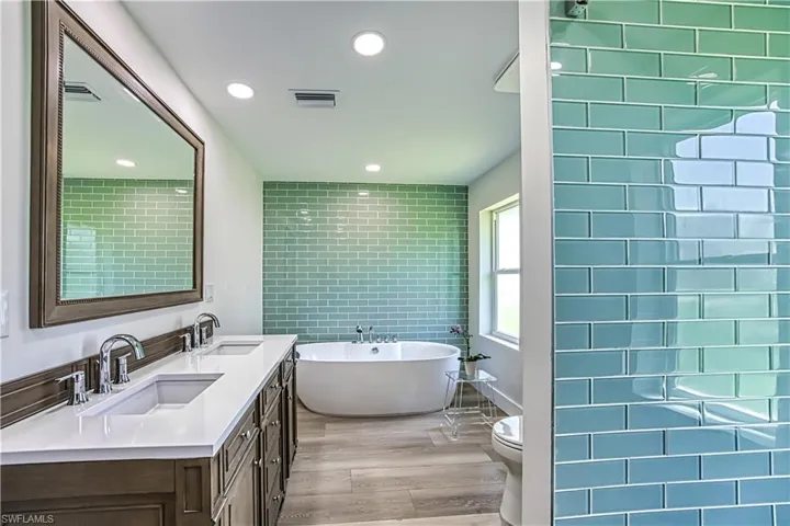 Full bathroom featuring light wood finished floors, double vanity, a freestanding bath, recessed lighting, and tile walls