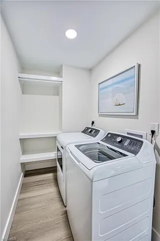 Washroom with light wood-type flooring and washing machine and clothes dryer