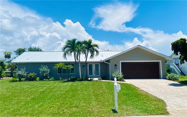 Ranch-style house on elevated lot featuring a metal roof, a front yard, a garage, and decorative driveway