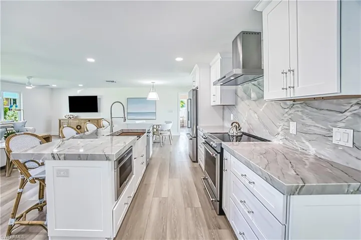 Kitchen with a breakfast bar, white cabinetry, appliances with stainless steel finishes, wall chimney exhaust hood, and light wood-type flooring