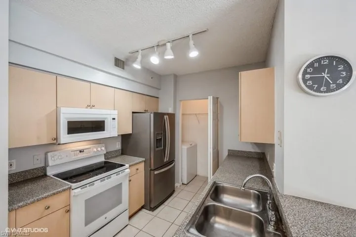 Kitchen featuring sink, a textured ceiling, light brown cabinetry, and white appliances