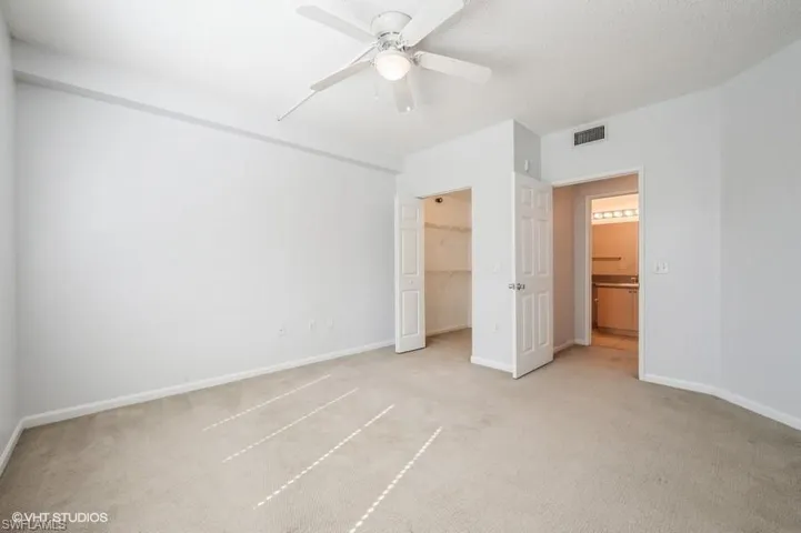 Unfurnished bedroom featuring ceiling fan, a textured ceiling, light carpet, a spacious closet, and a closet