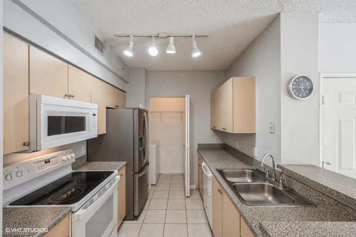 Kitchen with sink, white appliances, light tile patterned floors, and a textured ceiling