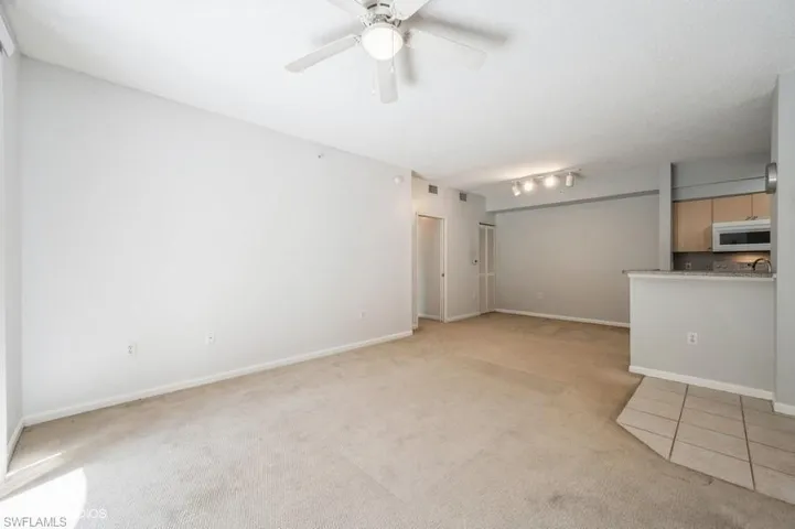 Unfurnished living room featuring light carpet, rail lighting, and ceiling fan