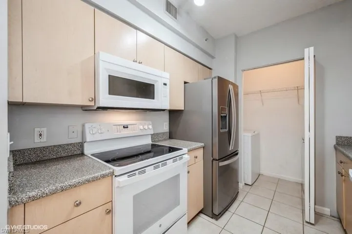 Kitchen with light tile patterned floors, white appliances, light brown cabinets, a textured ceiling, and washer and clothes dryer