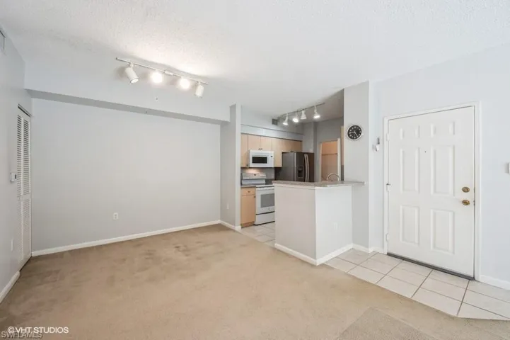 Kitchen featuring a textured ceiling, light carpet, light brown cabinetry, and white appliances