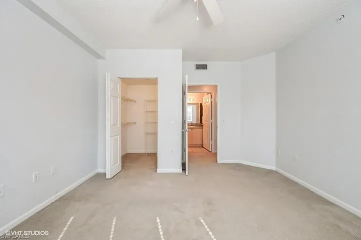 Unfurnished bedroom with a walk in closet, light colored carpet, ceiling fan, a textured ceiling, and a closet
