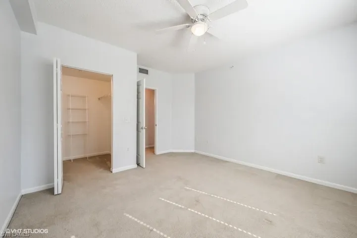 Unfurnished bedroom with a spacious closet, light carpet, a textured ceiling, a closet, and ceiling fan