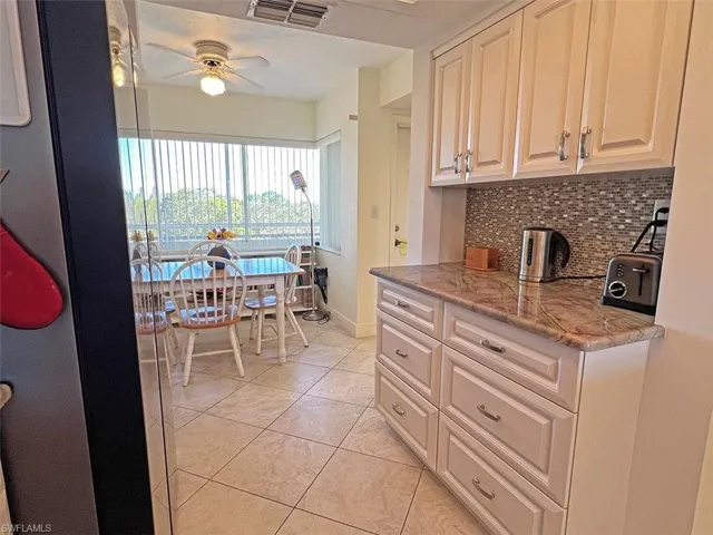 Kitchen with dark stone countertops, a ceiling fan, light tile patterned floors, and tasteful backsplash