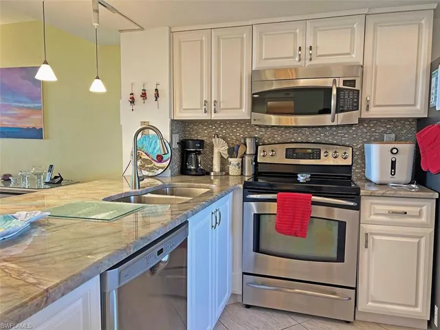 Kitchen featuring stainless steel appliances, pendant lighting, light stone counters, and white cabinets