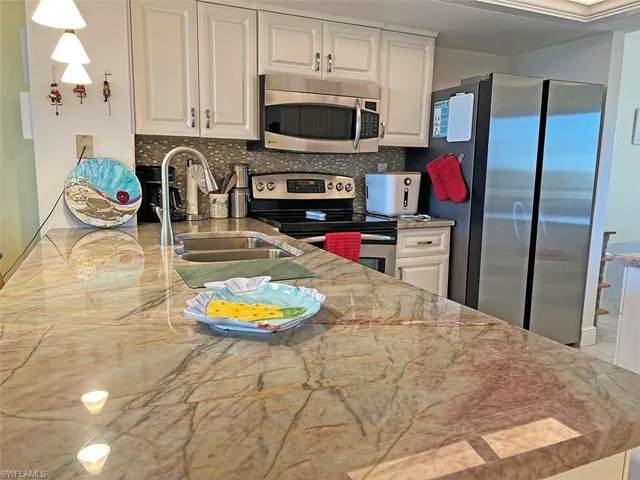 Kitchen with stainless steel appliances, backsplash, white cabinetry, and light stone countertops