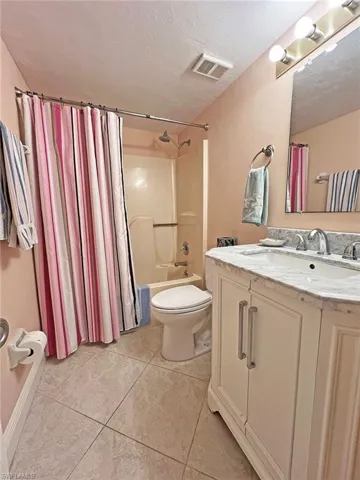 Bathroom featuring vanity, shower / bath combination with curtain, a textured ceiling, and light tile patterned floors