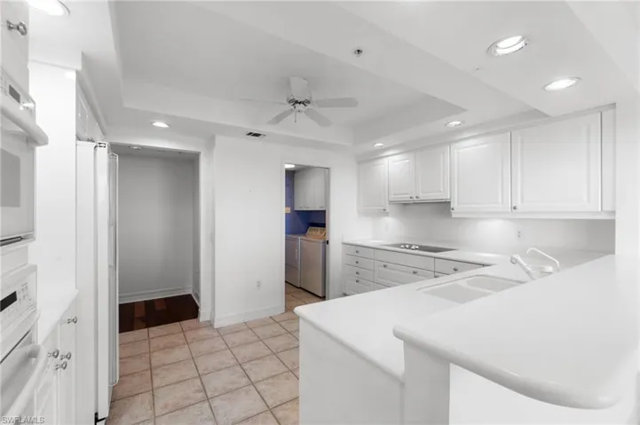 Kitchen with kitchen peninsula, ceiling fan, white cabinetry, independent washer and dryer, and sink