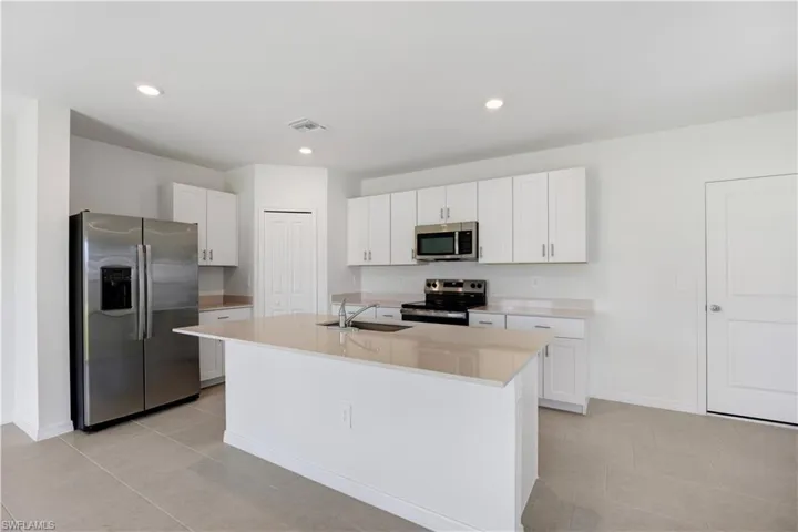 Kitchen featuring a center island with a sink, stainless steel appliances, recessed lighting, white cabinetry, and light-toned countertops