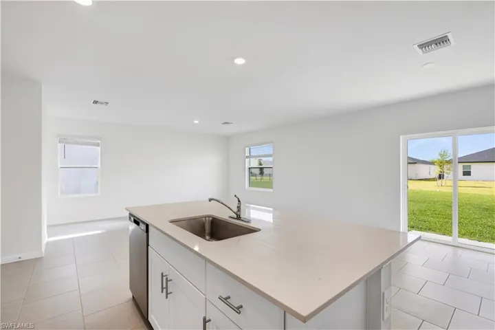 Kitchen island featuring a stainless steel sink, a modern faucet, and light-toned countertops