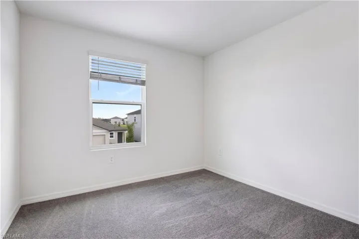 Room featuring a large window with horizontal blinds, neutral white walls, and dark grey carpeting