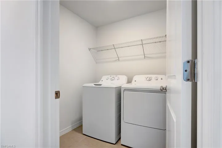 Dedicated laundry area featuring a wire storage shelf, tile flooring, and white baseboards