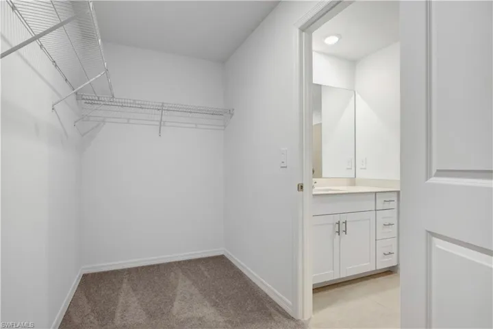 Walk-in closet featuring wire shelving, plush carpeting, and access to a full bathroom with a vanity, mirror, and recessed lighting
