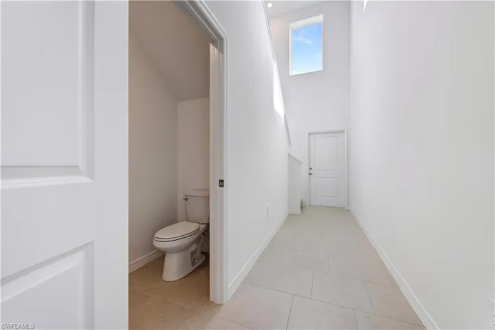 Two-panel interior door opening to a powder room with a standard toilet and light-toned floor tiling