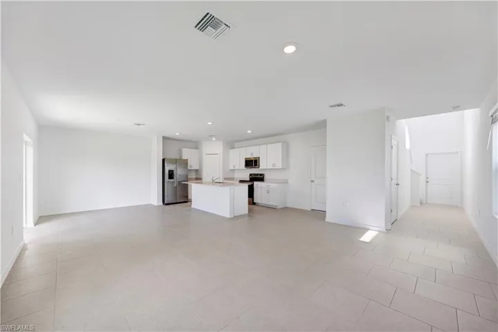 Open-concept living area featuring light-toned tile flooring, recessed lighting, and a kitchen island