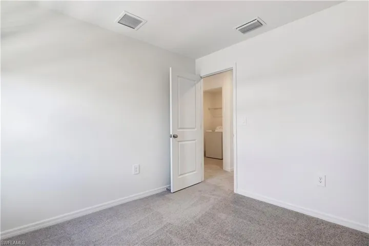 Carpeted interior room with white walls, white baseboards, and a white door leading to an interior laundry area