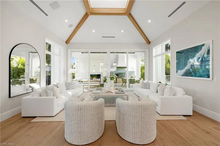 Living area featuring beamed ceiling, high vaulted ceiling, light wood-style flooring, a glass covered fireplace, and recessed lighting