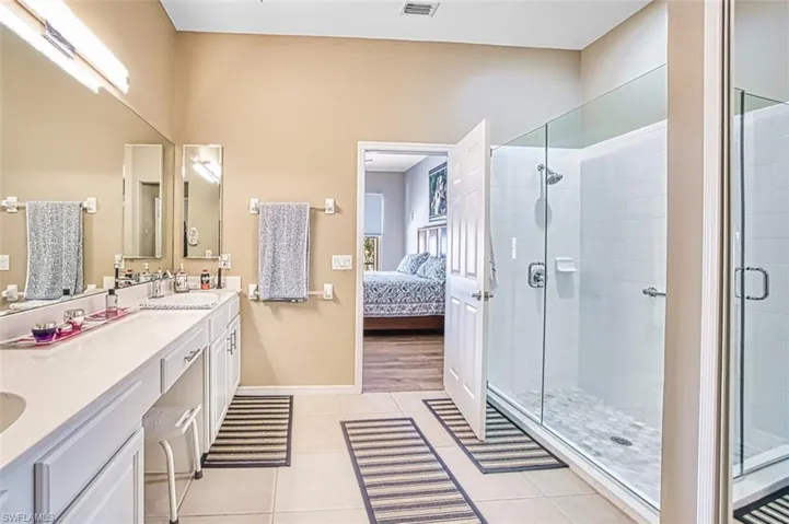 Full bathroom featuring connected bathroom, double vanity, a shower stall, and light tile patterned floors