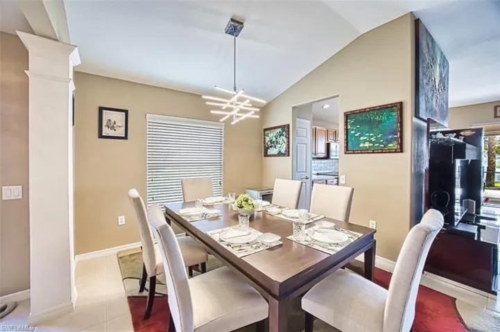 Dining room with vaulted ceiling, light tile patterned floors, ornate columns, and a chandelier