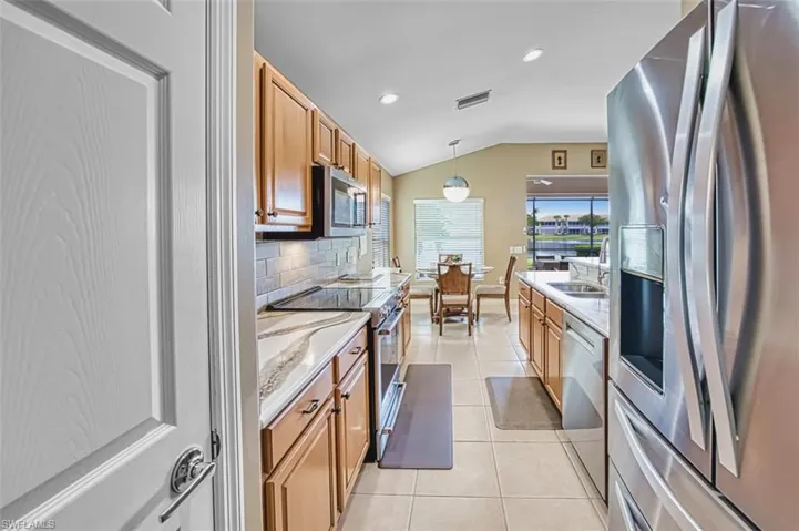 Kitchen featuring stainless steel appliances, light tile patterned floors, backsplash, hanging light fixtures, and vaulted ceiling