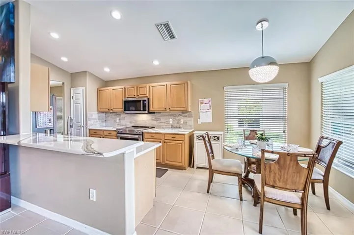 Kitchen with vaulted ceiling, backsplash, stainless steel appliances, decorative light fixtures, and light tile patterned flooring