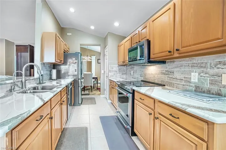 Kitchen featuring stainless steel appliances, light stone counters, lofted ceiling, light tile patterned flooring, and tasteful backsplash