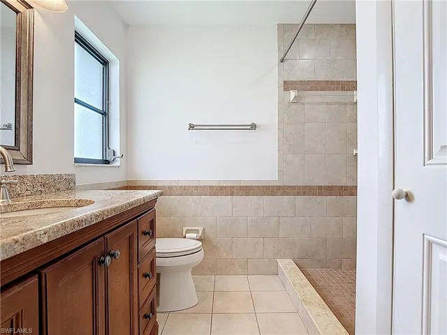 Bathroom with vanity, a tile shower, tile patterned floors, tile walls, and a wainscoted wall